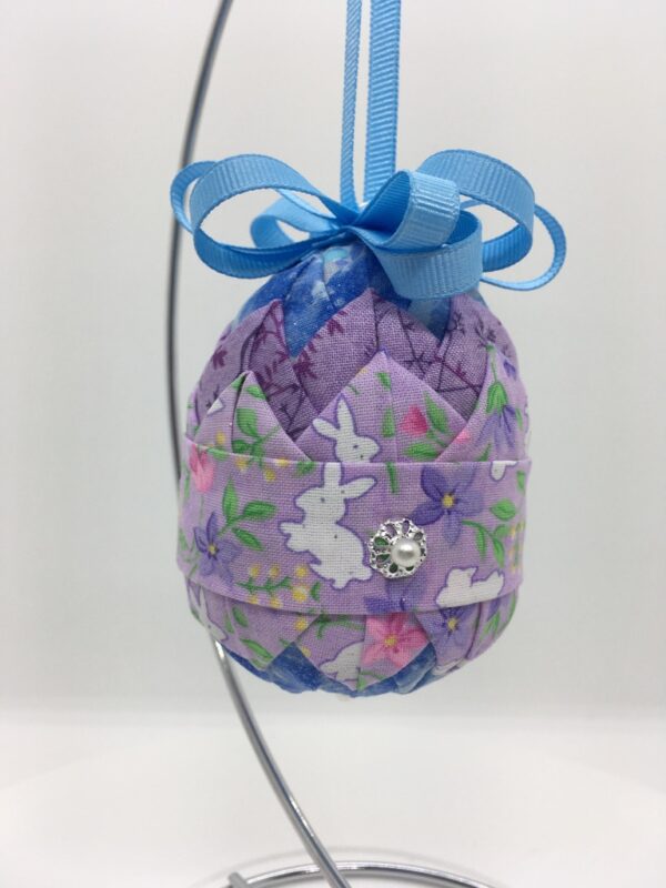 Lavender fabric with bunnies is pinned on a layer of darker purple fabric, on a three inch egg foam shape.