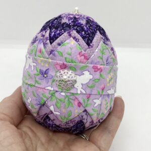Lavender fabric with bunnies is pinned on a layer of darker purple fabric, on a four inch egg foam shape.