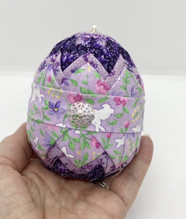 Lavender fabric with bunnies is pinned on a layer of darker purple fabric, on a four inch egg foam shape.