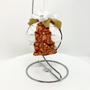 Pumpkin print fabric is folded to resemble a tree and is pinned on white fabric on a three inch round ball. It is topped with a gold bow and ribbon.