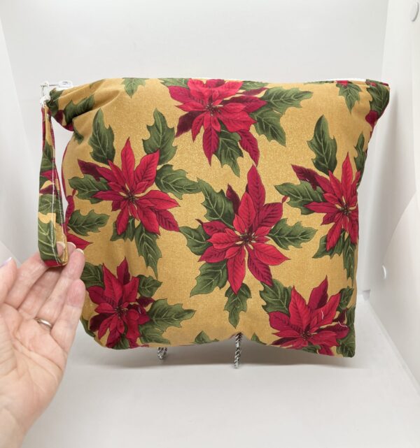 Eleven by thirteen inch project bag handcrafted with poinsettias on a sparkly gold background upcycled fabric. Has a zipper closure with an accessible handle attached to the zipper.