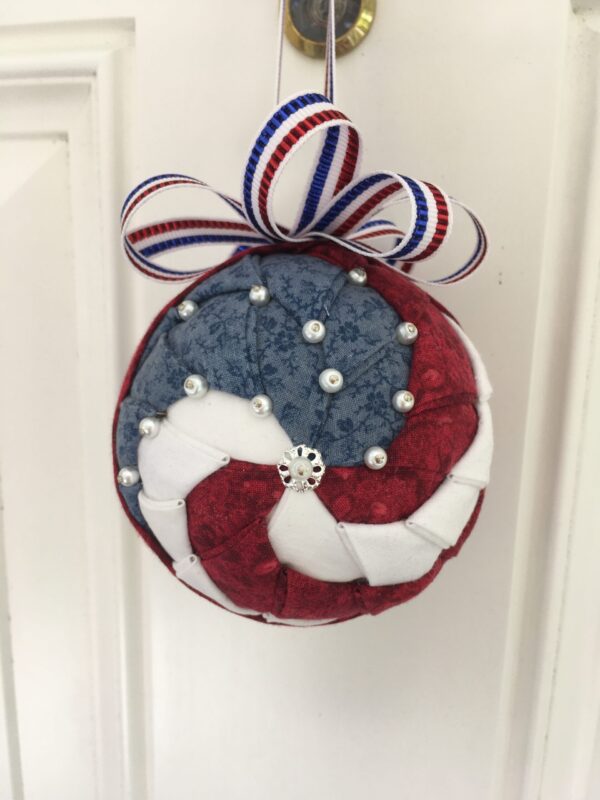 3" round ball patriotic spiral ornament, red, white & blue fabrics attached with pins. Pearlized white pins attached to simulate stars. Red, white & blue ribbon bow and hanger attached.