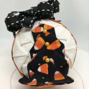Three inch round ornament made with folding and pinning fabrics on the a polystyeren ball. The candy corn fabric with black background are folded to resemble a tree. White fabric makes the backgroun and a pumpkin print is used as a band to separate one side from the other. It it topped with a black ribbon with white edging as a bow and hanger.