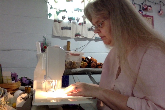 Woman at sewing machine with window behind her with train print curtains.