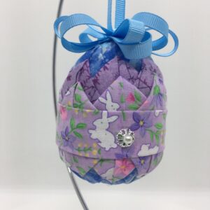 Lavender fabric with bunnies is pinned on a layer of darker purple fabric, on a three inch egg foam shape.