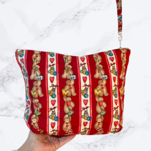 Eleven by thirteen inch project bag handcrafted with striped gingerbread figures dress as baker on a primarily red background. Has a zipper closure with an accessible handle attached to the zipper.