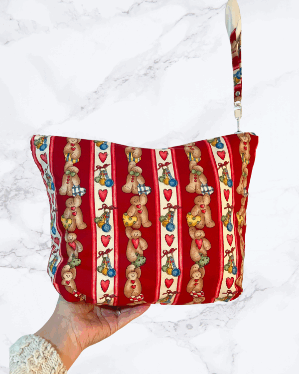 Eleven by thirteen inch project bag handcrafted with striped gingerbread figures dress as baker on a primarily red background. Has a zipper closure with an accessible handle attached to the zipper.