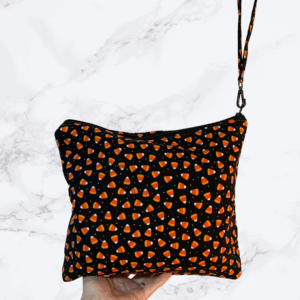 Eleven by thirteen inch project bag handcrafted with candy corn print fabric on a black background. Has a zipper closure with an accessible handle attached to the zipper.