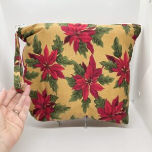 Eleven by thirteen inch project bag handcrafted with poinsettias on a sparkly gold background upcycled fabric. Has a zipper closure with an accessible handle attached to the zipper.