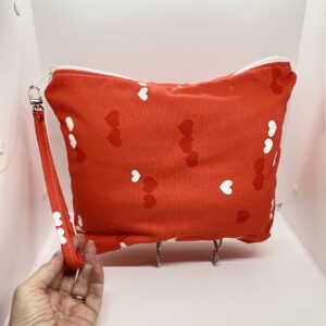 Eleven by thirteen inch project bag handcrafted with red and white hearts on a red background upcycled fabric. Has a zipper closure with an accessible handle attached to the zipper.